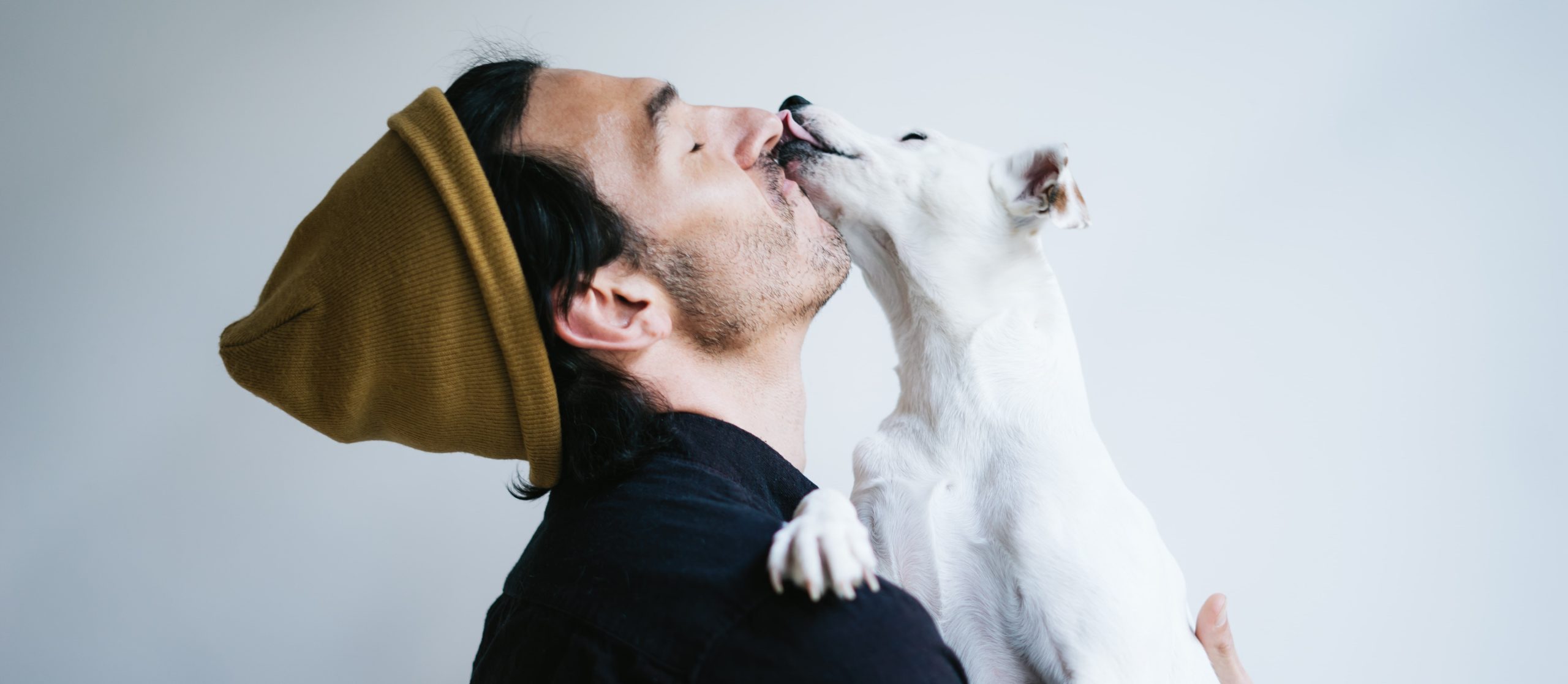 Ein Jack Russell Terrier leckt einem Mann über die Nase. Der Mann küsst den Hund am Hals.